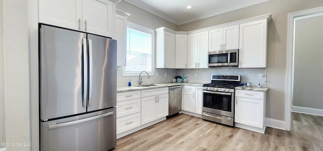 kitchen with tasteful backsplash, white cabinets, appliances with stainless steel finishes, ornamental molding, and a sink