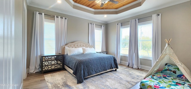 bedroom featuring ornamental molding, light wood-type flooring, a raised ceiling, and baseboards