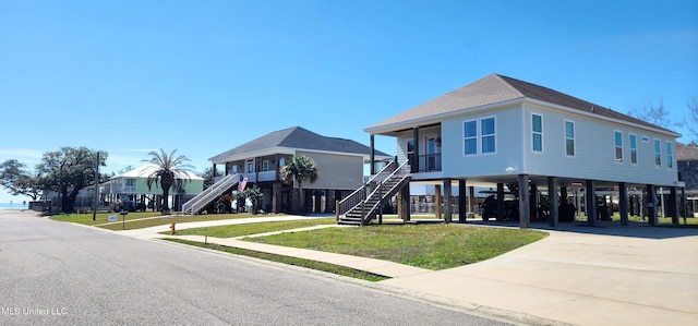 beach home featuring covered porch, driveway, stairway, a carport, and a front yard