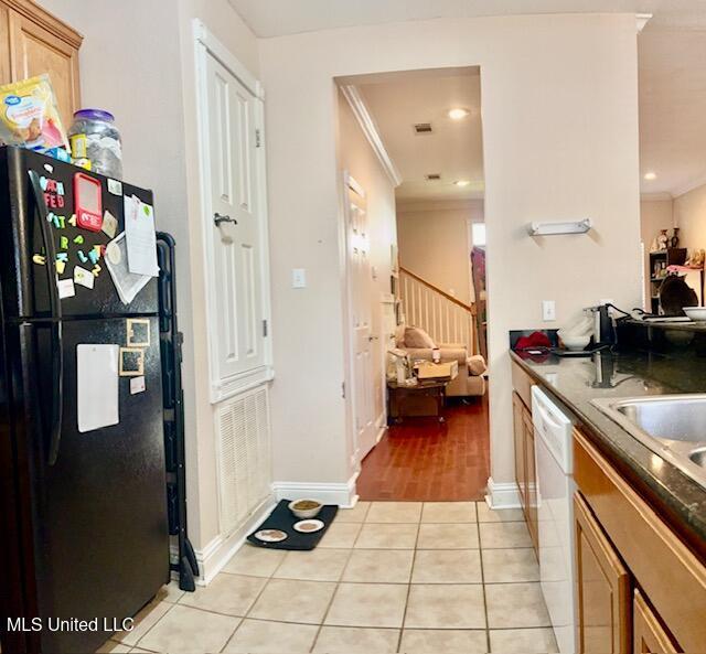 kitchen featuring light tile patterned flooring, white dishwasher, black fridge, and crown molding