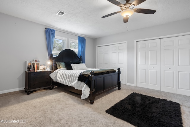 carpeted bedroom featuring a textured ceiling, two closets, and ceiling fan