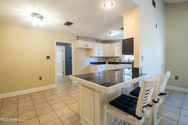 kitchen with white cabinetry, tile counters, kitchen peninsula, a breakfast bar area, and light tile patterned flooring