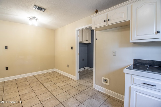 clothes washing area featuring light tile patterned floors, cabinets, a textured ceiling, and washer hookup