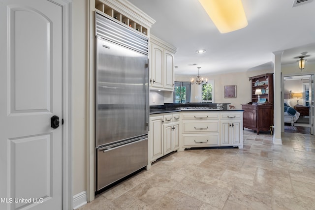 kitchen featuring an inviting chandelier, cream cabinetry, built in fridge, and hanging light fixtures