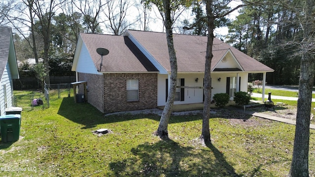 view of front facade with fence, cooling unit, roof with shingles, a front yard, and brick siding