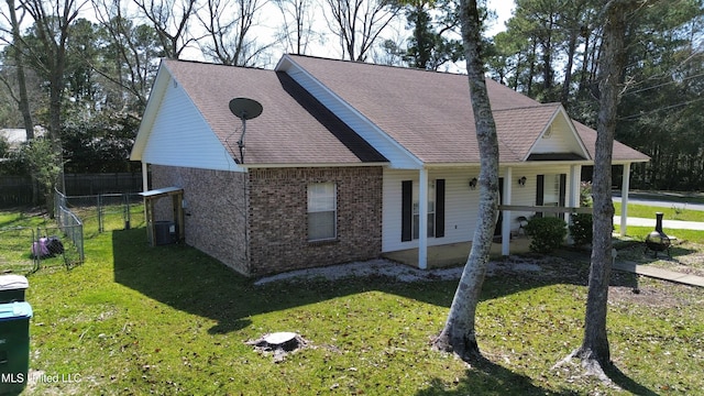 view of front facade with brick siding, a shingled roof, a front yard, and fence