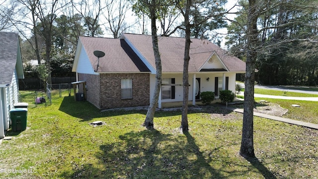 view of front facade featuring a front yard, central AC unit, fence, roof with shingles, and brick siding