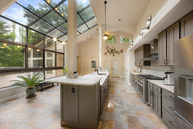 6821 Autumn Oaks Dr, Olive Branch, MS 38654 - kitchen featuring wall chimney exhaust hood, stone tile floors, appliances with stainless steel finishes, decorative backsplash, and a center island with sink