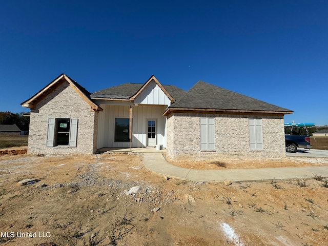 view of front of home with board and batten siding, brick siding, and roof with shingles