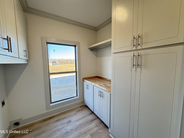 clothes washing area with cabinet space, baseboards, crown molding, light wood-type flooring, and electric dryer hookup