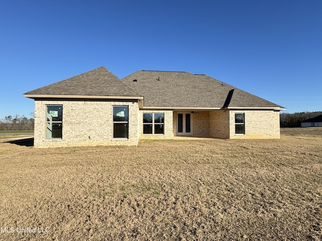 back of house with brick siding, roof with shingles, a lawn, and french doors