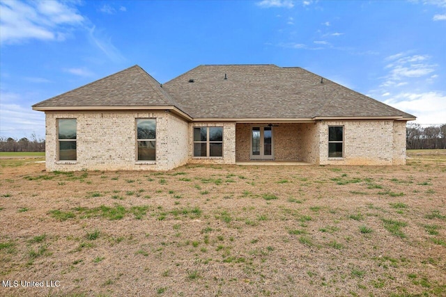 back of house with a lawn, french doors, roof with shingles, and brick siding