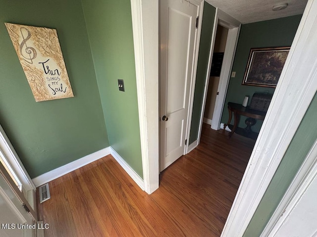 hall with baseboards, visible vents, wood finished floors, and a textured ceiling