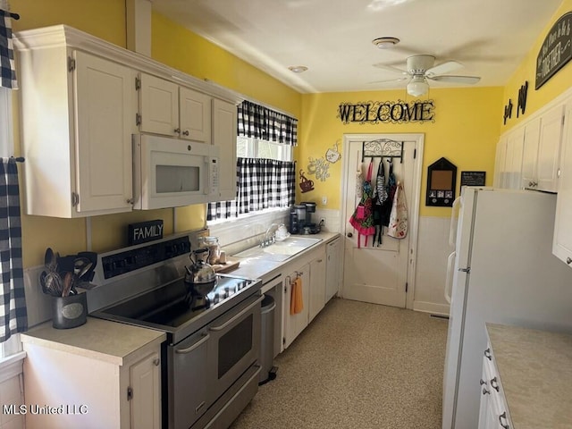 kitchen with a wainscoted wall, light countertops, a sink, white appliances, and ceiling fan