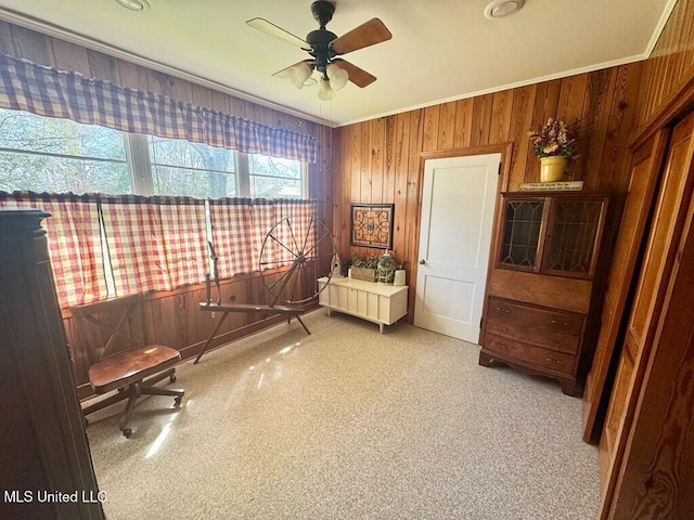 living area featuring a ceiling fan, crown molding, and wooden walls