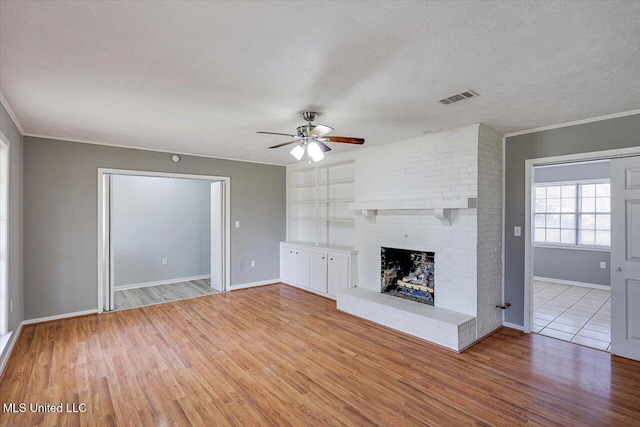 unfurnished living room featuring visible vents, a textured ceiling, a brick fireplace, and wood finished floors