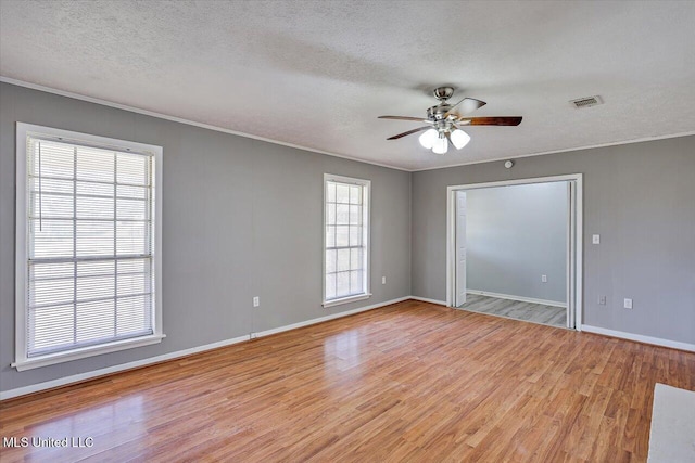 empty room with visible vents, light wood-style floors, ornamental molding, and a textured ceiling