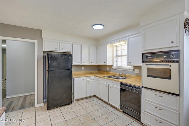 kitchen featuring black appliances, a sink, white cabinetry, light countertops, and light tile patterned floors