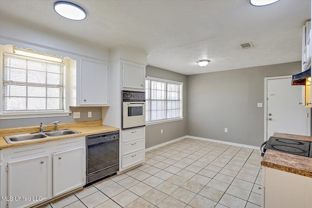 kitchen with light tile patterned flooring, a sink, white cabinets, wall oven, and dishwasher