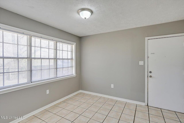 empty room featuring light tile patterned floors, a textured ceiling, and baseboards