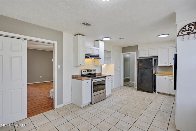 kitchen featuring freestanding refrigerator, stainless steel range with electric cooktop, a barn door, white cabinets, and light tile patterned floors