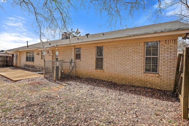 rear view of property with brick siding, a chimney, a patio, and fence