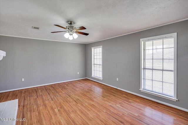 spare room featuring visible vents, light wood-style flooring, a textured ceiling, crown molding, and baseboards