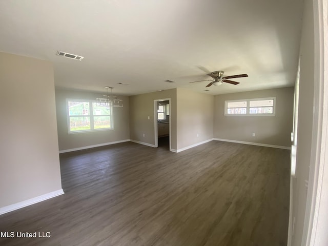 empty room with dark wood-style floors, visible vents, ceiling fan, and baseboards