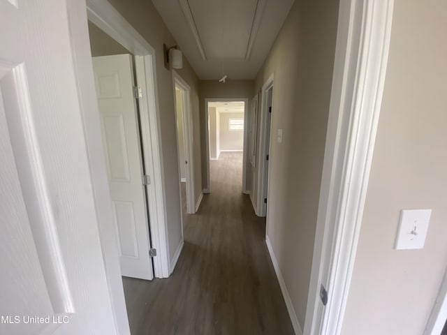 hallway with baseboards, attic access, and dark wood finished floors