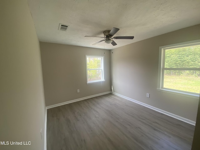 spare room featuring visible vents, baseboards, a textured ceiling, and dark wood-style flooring