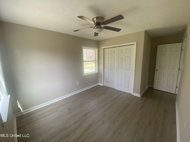 unfurnished bedroom with a ceiling fan, dark wood-style floors, baseboards, a closet, and a textured ceiling