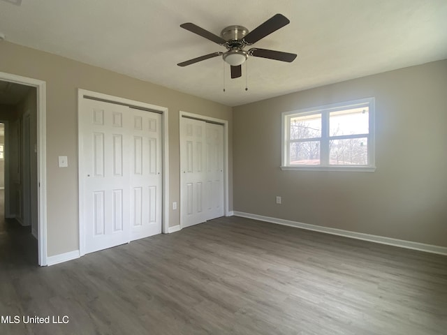 unfurnished bedroom featuring two closets, dark wood-type flooring, baseboards, and a ceiling fan