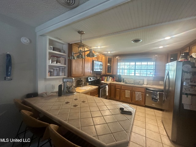 kitchen featuring black appliances, tile countertops, kitchen peninsula, pendant lighting, and light tile patterned floors