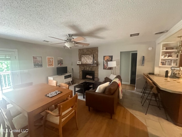 living room with a fireplace, a textured ceiling, light wood-type flooring, and ceiling fan