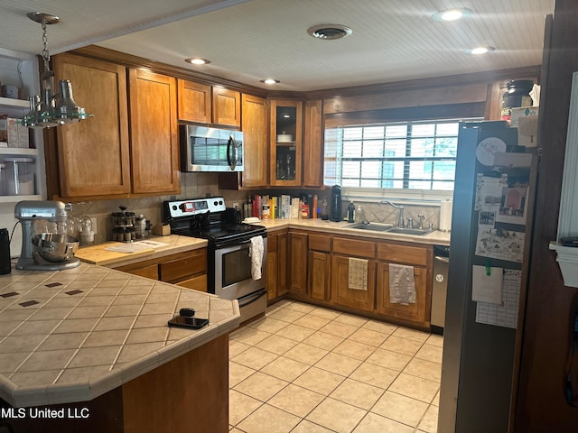 kitchen with kitchen peninsula, hanging light fixtures, sink, tile counters, and stainless steel appliances