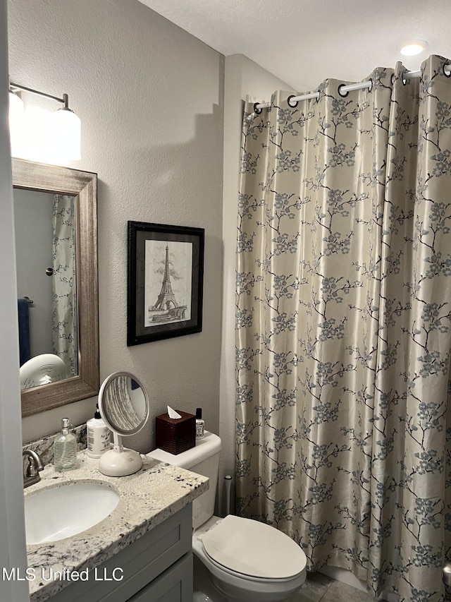 bathroom featuring toilet, curtained shower, a textured wall, and vanity