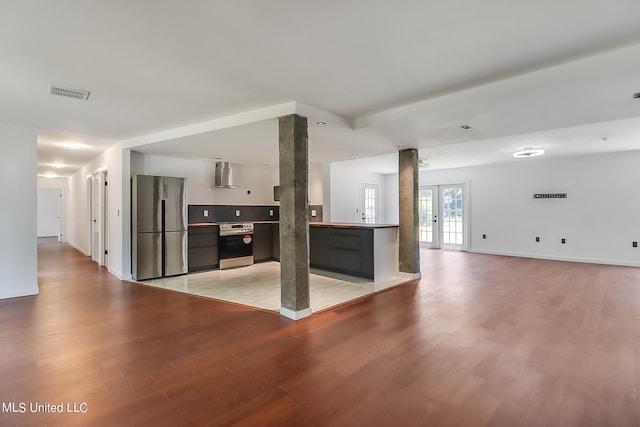 kitchen featuring appliances with stainless steel finishes, light hardwood / wood-style flooring, french doors, and wall chimney range hood