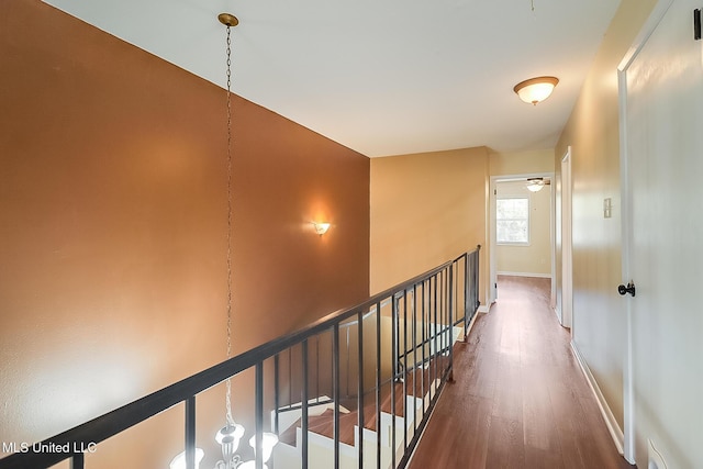 corridor with an upstairs landing, baseboards, and wood finished floors