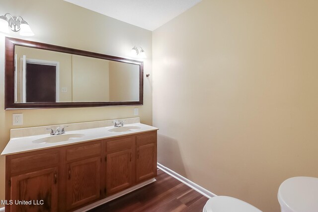 bathroom with double vanity, toilet, wood finished floors, and a sink