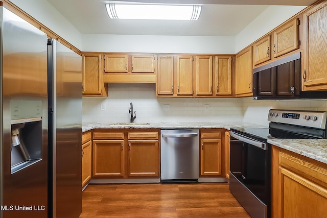 kitchen with a sink, appliances with stainless steel finishes, decorative backsplash, light stone countertops, and dark wood-style flooring