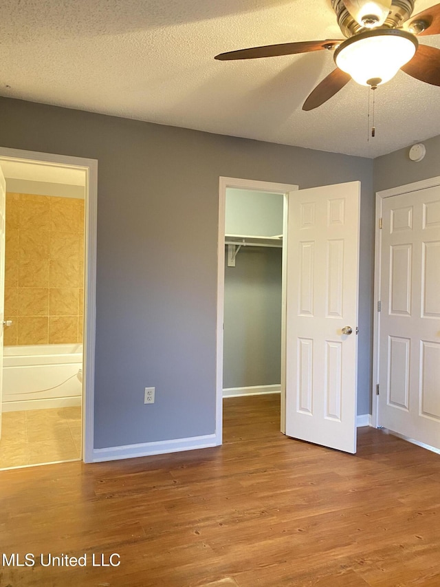 unfurnished bedroom featuring hardwood / wood-style flooring, a spacious closet, a textured ceiling, ensuite bath, and a closet