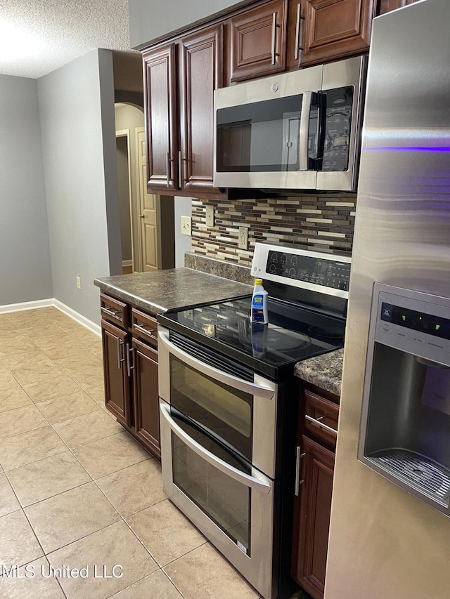 kitchen with light tile patterned flooring, dark brown cabinetry, tasteful backsplash, a textured ceiling, and stainless steel appliances