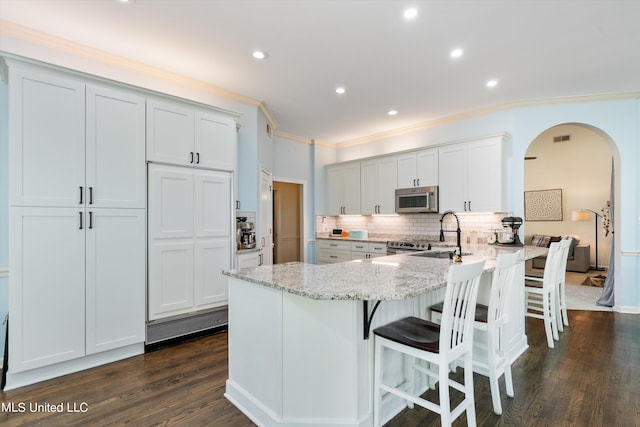 kitchen with light stone countertops, ornamental molding, dark wood-type flooring, sink, and stainless steel appliances