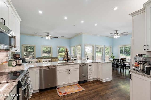 kitchen featuring dark wood-type flooring, kitchen peninsula, ornamental molding, white cabinets, and appliances with stainless steel finishes