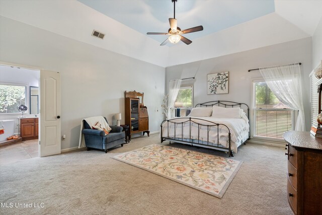 carpeted bedroom featuring ceiling fan, lofted ceiling, multiple windows, and ensuite bath