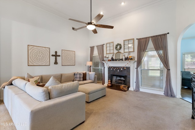 carpeted living room with ornamental molding, a high ceiling, a fireplace, and ceiling fan