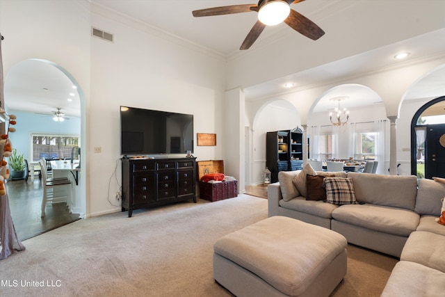 living room featuring light carpet, ornamental molding, ceiling fan with notable chandelier, and a towering ceiling