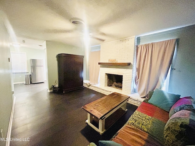 living room with ceiling fan, hardwood / wood-style floors, a textured ceiling, and a brick fireplace