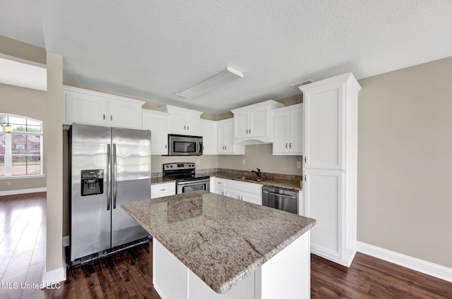 2338 Khushboo Cv, Southaven, MS 38671 - kitchen featuring stainless steel appliances, a kitchen island, dark wood-style floors, white cabinetry, and light stone counters