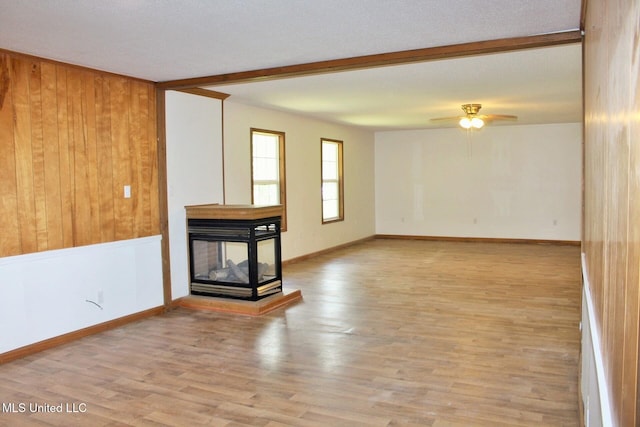 unfurnished living room with baseboards, a ceiling fan, wood walls, and wood finished floors